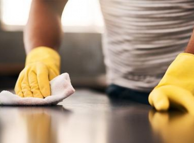 Close up of hands in yellow gloves wiping down a table